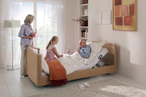 Evde sağlık hizmeti alan bir hastanın yanında doktorun kontrol yapması ve not alması.