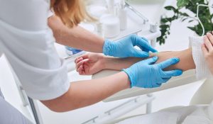 Evde hemşire tarafından kan örneği alınan yaşlı ve yoğun iş temposuna sahip bir hasta.