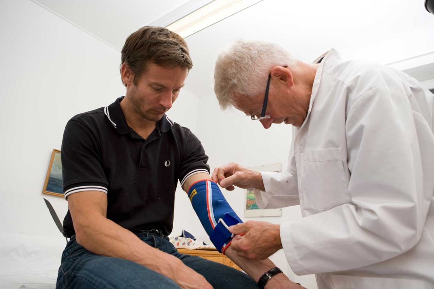 Evde muayenede doktorun tansiyon ölçmesi ve hastanın notlarını kontrol etmesi.