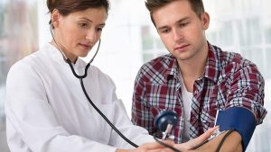 Evde muayenede doktorun yaşlı hastayı dinleyip tansiyonunu ölçmesi, yakınının yanında bilgi vermesi.