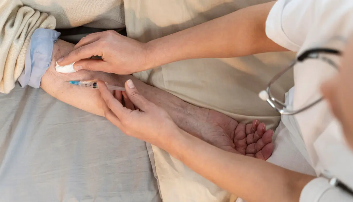 Evde sağlık personelinin hastaya damar yolu açıp serum bağladığı, yanında tansiyon aleti bulunan bir sahne.