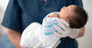 Koltukta huzurla kahvesini yudumlayıp dinlenen anne ve o sırada bebeğin uykuya dalmasına yardımcı olan şefkatli bebek hemşiresi.